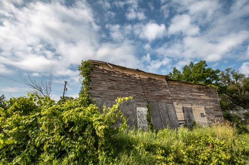 An abandoned wooden house in a grassy field under the cloudy sky