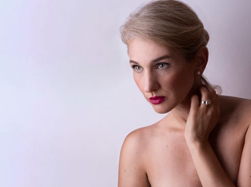 A blonde middle-aged Caucasian woman posing naked on a light purple background