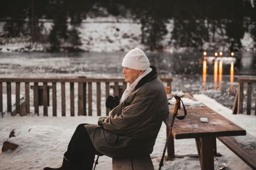 Senior man sitting at snowy table by frozen lake in Black Forest, Germany