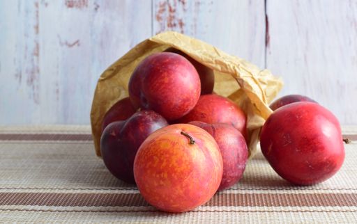 Fresh ripe plums inside a kraft paper bag on a tablecloth