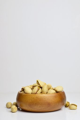 A wooden bowl with tasty pistachios isolated on a white background - dried seeds