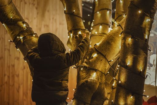 Child in winter coat decorating tree with lights during festive season, creating a warm and cozy atmosphere.