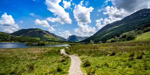A panoramic shot of a lake surrounded by mountainous landscape with a roa
