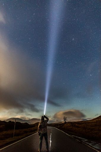 A vertical shot of a road and a male standing under the stars