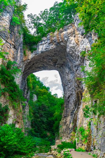 Stunning view of Natural Bridge in Virginia, showcasing the grand rock formation surrounded by lush greenery and a serene path.