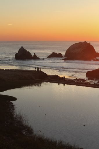 A vertical shot of the rocky coast of Sutro baths with people at sunset in San Francisco
