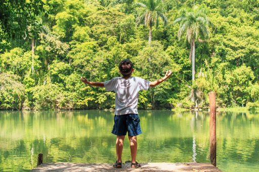 A young boy standing on the pier with arms wide open in La Arboleda protected area, Matanzas, Cuba