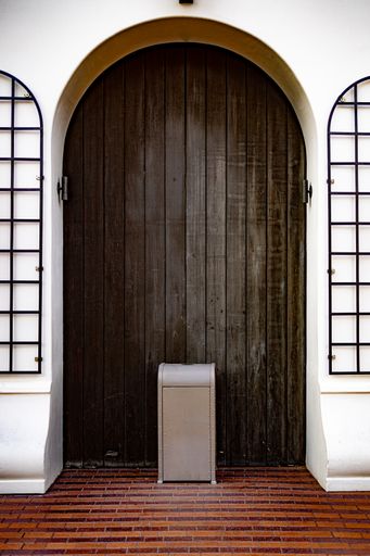 A vertical shot of a trashcan in front of a wooden door, on a brick floor