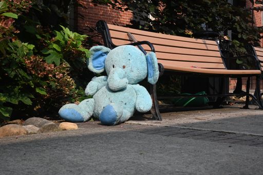 An old dirty elephant toy by a bench in a park