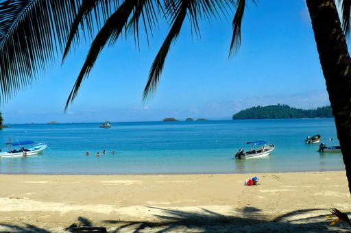 The calm sea with people swimming and driving boats from sandy, sunny shore