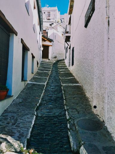 A vertical shot of an alley with white buildings and a runnel captured on a sunny day
