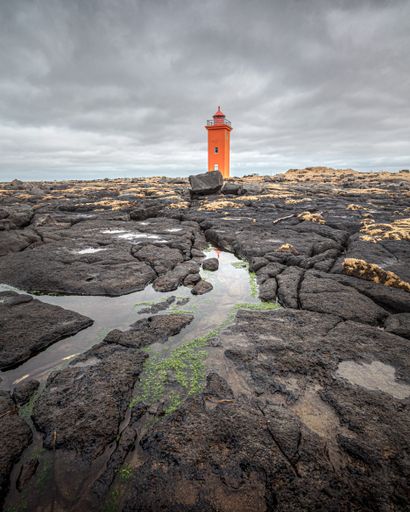 A beautiful view of an orange lighthouse under the cloudy sky