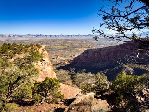 Canyon rim trail view with cliffs trees distant mountains and blue sky in colorado national monument