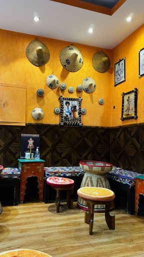 Colorful traditional interior with woven hats and ethnic decor on orange walls, featuring wooden stools and tables in a cozy setting.