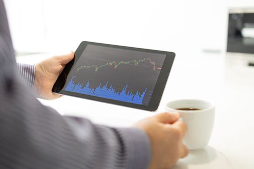 Retail trader looking at a digital tablet with stock market chart and holding a cup of coffee in a modern kitchen. Trading at home concept
