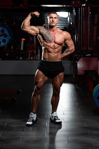 A man standing strong in the gym and flexing muscles; athletic fitness model posing after exercises