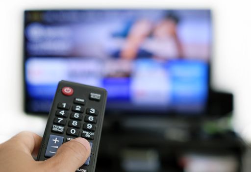 Hand holding remote control and a TV screen in the background - binge watching the favourite TV show