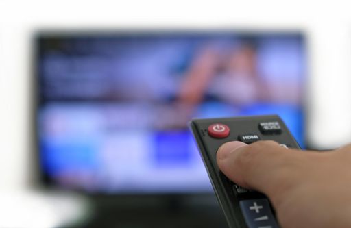 Hand holding remote control and a TV screen in the background - binge watching the favourite TV show
