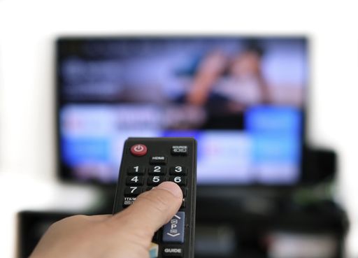 Hand holding remote control and a TV screen in the background - binge watching the favourite TV show