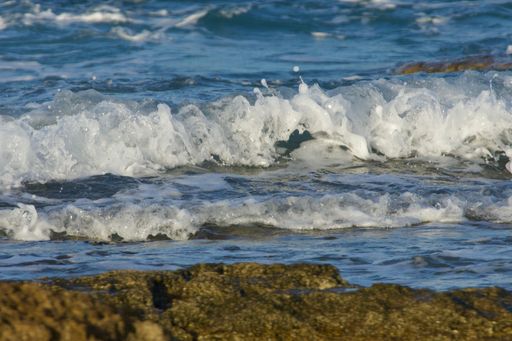 Waves crashing on rocky shore with blue ocean backdrop, capturing the essence of coastal beauty.