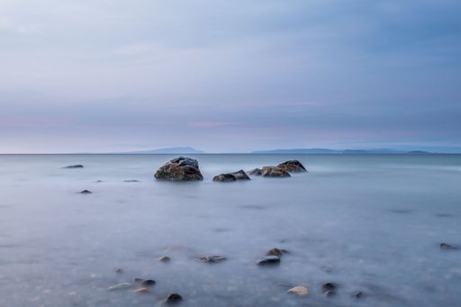 Serene seascape with rocks emerging from calm water under a pastel sky, capturing tranquility and nature's beauty.