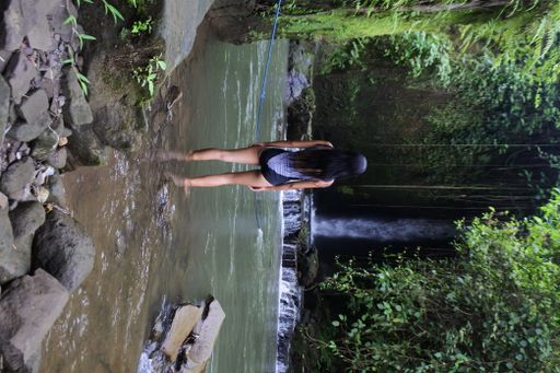 A flipped vertical shot of a lady wearing a swimsuit standing on a rock admiring the waterfall