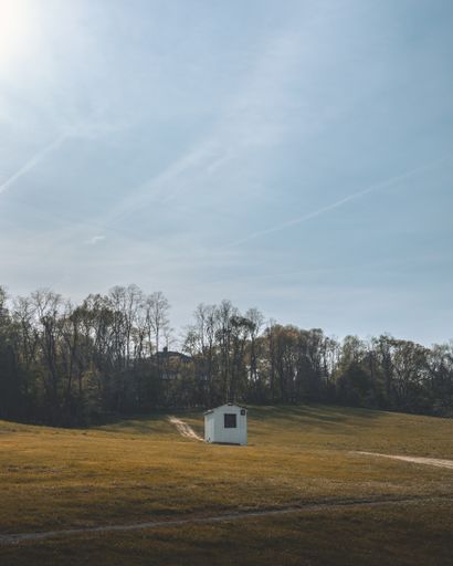 A vertical shot of a tiny white house in a field during the day under the clear skies