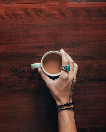A top view shot of a female's hand holding a white cup full of coffee on a wooden surface