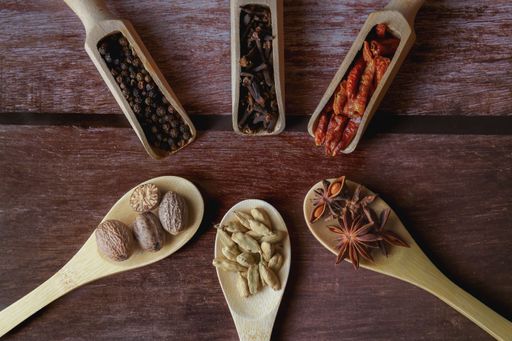 Various whole spices and dried herbs creating a flavorful cooking ingredient collection on rustic wooden background