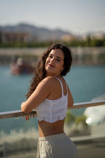 Young woman with curly hair in a white top enjoying a sunny day by the waterfront.