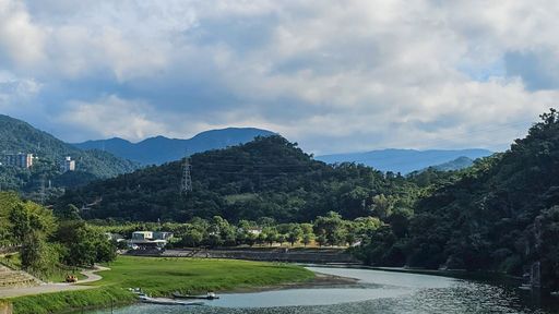 Scenic view of lush green hills and a winding river under a partly cloudy sky, capturing the tranquility of nature.