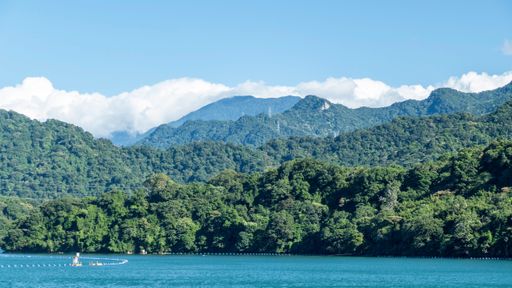 Scenic view of lush green mountains and clear blue water under a bright sky, capturing the tranquility of nature.