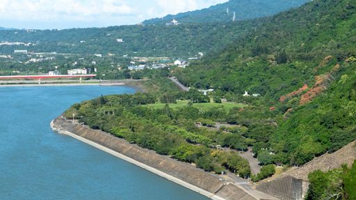 Scenic view of lush green hills and a serene river under a clear sky, creating a tranquil natural landscape.