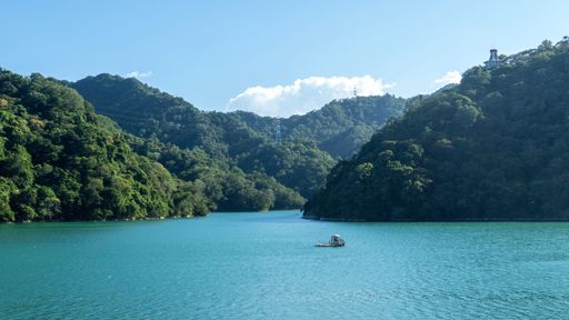 Scenic view of a tranquil lake surrounded by lush green hills under a clear blue sky, perfect for nature and travel themes.