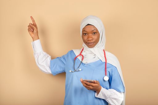 A young Muslim nurse holding a smartphone and pointing her finger up