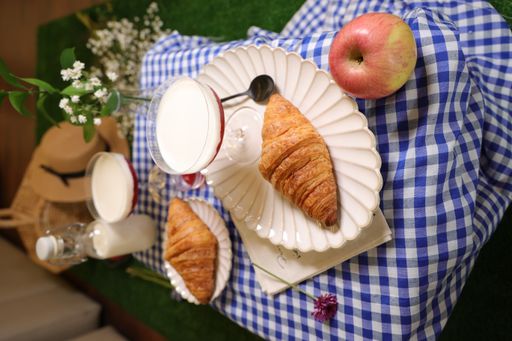 A vertical shot of fresh croissants with a sweet dessert, jam and apple outdoors in the park