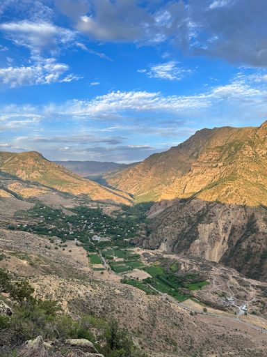 A stunning view of a lush valley nestled between rugged mountains under a vibrant blue sky with scattered clouds.
