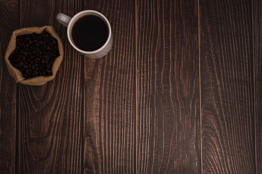 A closeup shot of a cup of coffee and roasted beans in a burlap sack on wooden surface