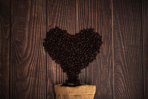 A top view of heart-shaped roasted coffee beans from a burlap sack