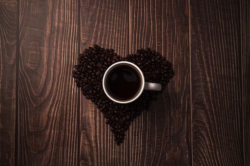 A top view of a cup of coffee with heart-shaped roasted coffee beans on the table