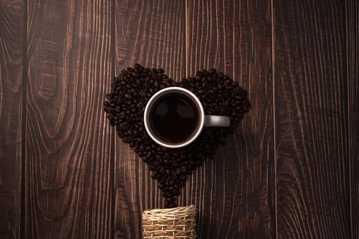 A cup of coffee with heart-shaped roasted coffee beans from a basketon the table