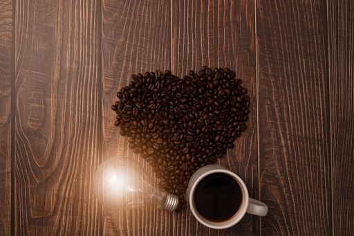 A top view of a cup of coffee with heart-shaped roasted coffee beans on the table