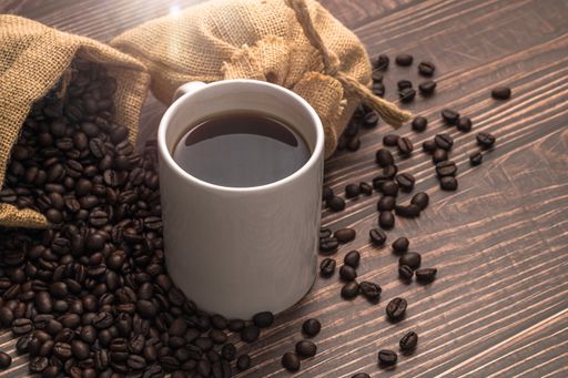 A cup of coffee with heart-shaped roasted coffee beans from a burlap sack on the table