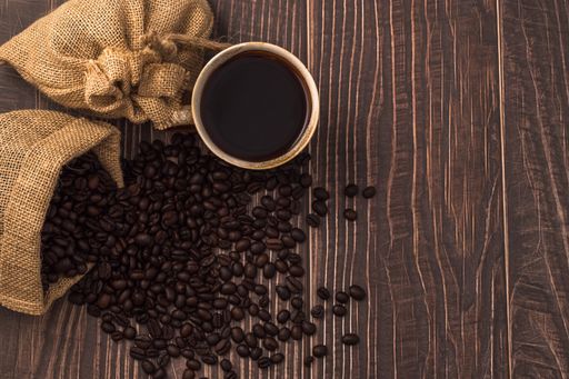 A cup of coffee with heart-shaped roasted coffee beans from a burlap sack on the table