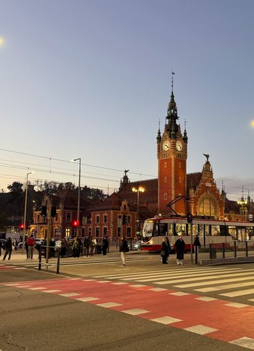 Evening scene of Gdansk Main Station with tram and people crossing the street. City life and architecture.