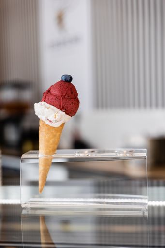 A vertical shot of vanilla and berry ice cream cone with a blueberry on top