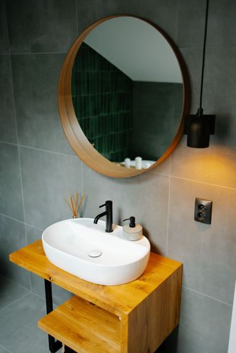 Modern bathroom interior with a round mirror, wooden vanity, and stylish sink, featuring a black faucet and ambient lighting.
