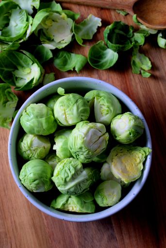 Fresh Brussels sprouts in a bowl on a wooden table, surrounded by loose leaves, showcasing vibrant green colors and healthy food concept.