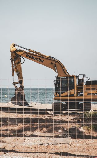 Yellow excavator digging at a coastal construction site by the sea