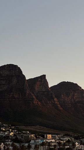 Scenic view of Twelve Apostles mountain range during sunset in Cape Town with clear sky and urban landscape below.